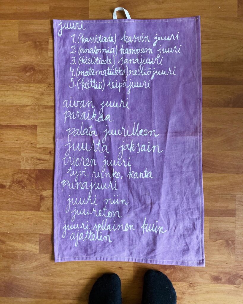 Lattialla violetiksi maalattu keittiöpyyhe, jossa sanan juuri sanakirjamerkityksiä.
